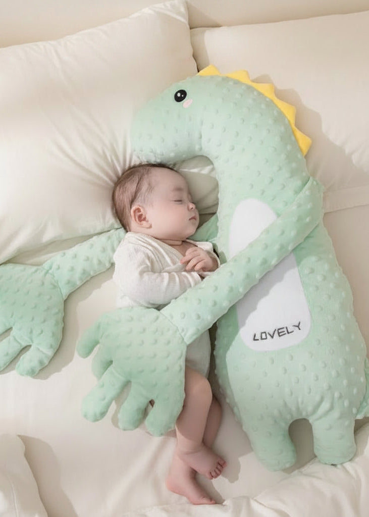 Baby lying on a green dinosaur-shaped pillow with 'LOVELY' text on a beige background.